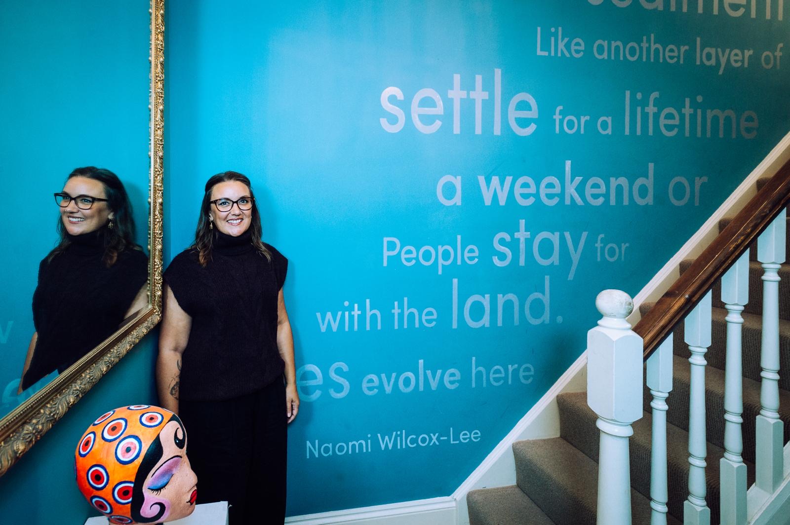 A guest smiles beside a turquoise stairwell painted with a poem by Naomi Wilcox-Lee