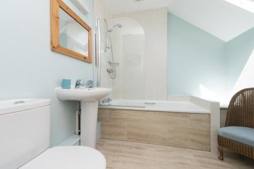 Pale blue attic bathroom with a bath, shower and wicker chair