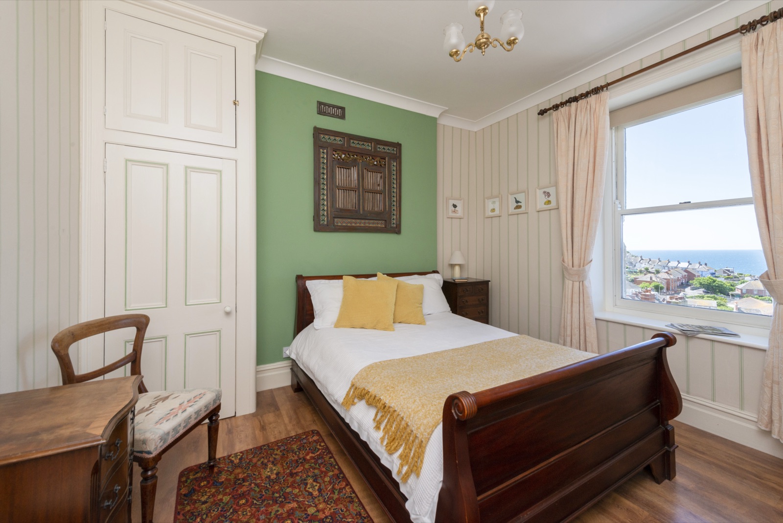 Double bedroom with a sleigh bed, yellow throw and a window looking over the rooftops to the sea