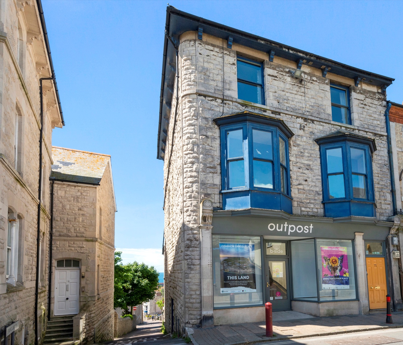 The stone-built b-side building at 77 Fortuneswell with blue bay windows and the sea beyond