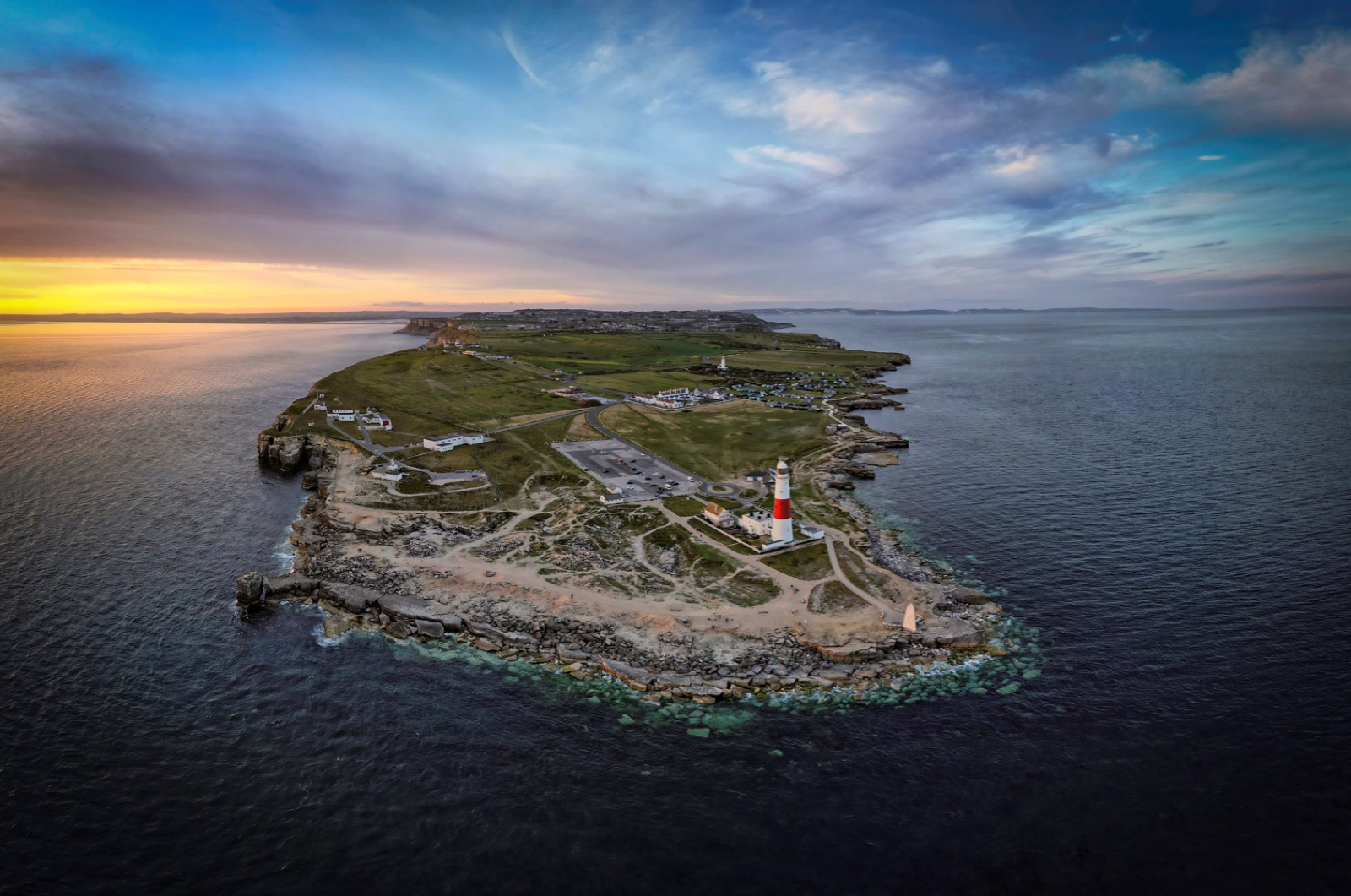 Portland Bill and its red and white lighthouse at dusk, seen from the air